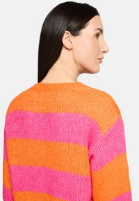 Pull en maille épaisse avec de larges rayures horizontales orange et rose. Coupe ample avec un col rond et un tissage texturé.