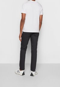 Camiseta blanca de manga corta, pantalones negros ajustados y zapatillas gris con acentos negros. Las telas parecen suaves; la camiseta tiene un sutil detalle de logo.