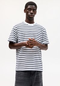 Gestreiftes T-Shirt aus weißer und marineblauer Baumwolle; Rundhalsausschnitt, kurze Ärmel, lockere Passform, mit gleichmäßig über den Stoff verlaufenden horizontalen Streifen.