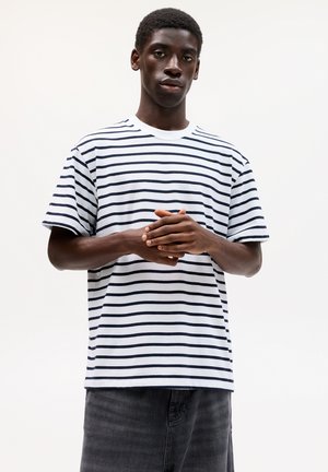 T-shirt rayé en coton blanc et bleu marine ; col rond, manches courtes, coupe décontractée, avec des rayures horizontales régulièrement espacées sur le tissu.