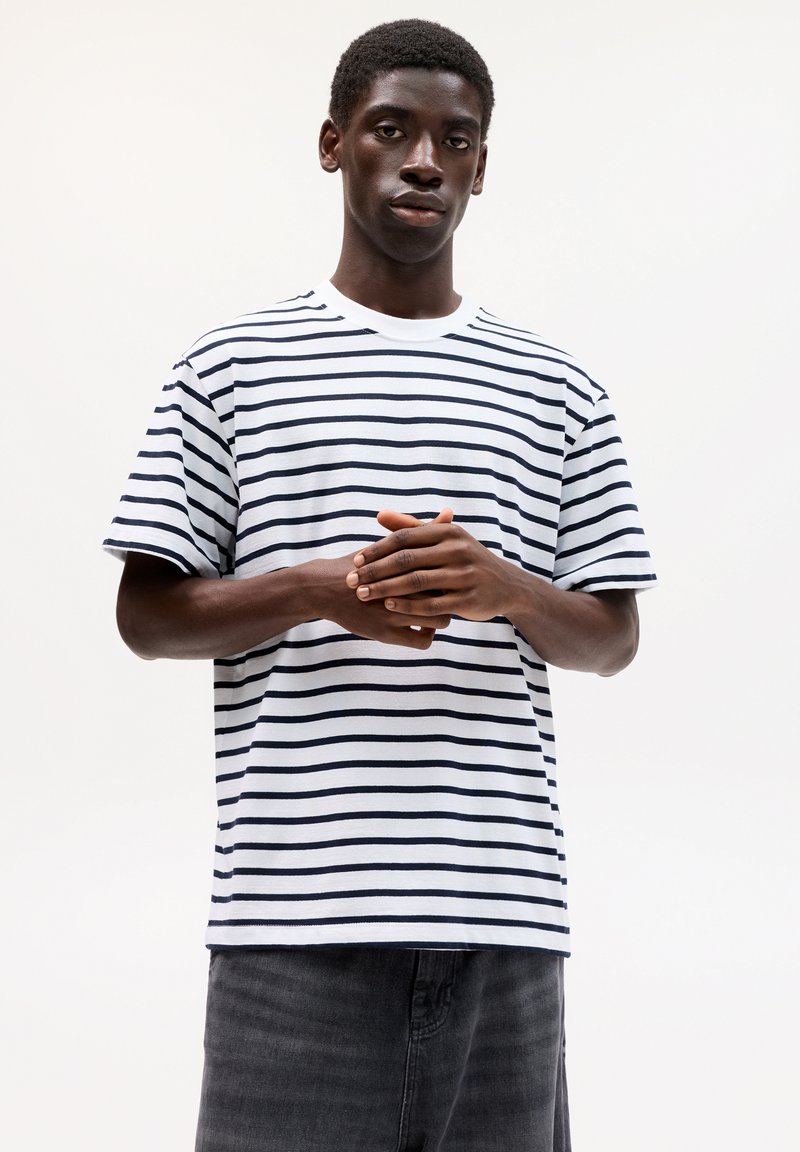 Gestreiftes T-Shirt aus weißer und marineblauer Baumwolle; Rundhalsausschnitt, kurze Ärmel, lockere Passform, mit gleichmäßig über den Stoff verlaufenden horizontalen Streifen.