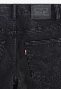 Jeans in denim nero con una finitura texture, caratterizzati da un'etichetta Levi's sulla vita e un'etichetta rossa sulla tasca posteriore. Due tasche posteriori visibili.