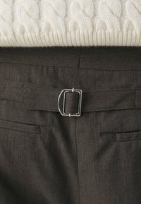 Pantalon gris foncé avec ceinture en tissu ajustable et boucle rectangulaire argentée, associé à un pull crème en maille torsadée.