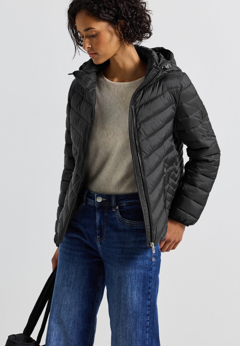 Svart vadderad pufferjacka med huva, dragkedja framtill och ribbade ärmar, bärs över en grå topp och matchas med blå vida jeans.