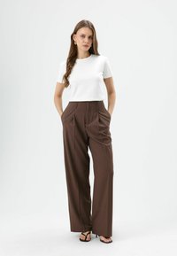 Haut blanc à manches courtes associé à un pantalon marron taille haute à jambes larges. Le tissu semble lisse avec de subtiles plis et une coupe ajustée.