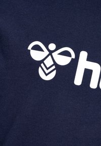 Țesătura din bumbac de culoare bleumarin prezintă un logo alb de albină cu aripi simetrice și modele în zig-zag, alături de cuvântul "hey" scris cu litere albe, îndrăznețe.