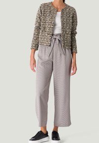 Gestreepte beige en zwarte geblokte jas, witte top, grijs geruite broek met strikceintuur en zwarte sneakers. Casual outfit.