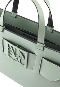 Borsa a mano verde in ecopelle con manici doppi, chiusura con zip e una placca con logo testurizzata. Presenta una tasca interna e accenti neri a contrasto.