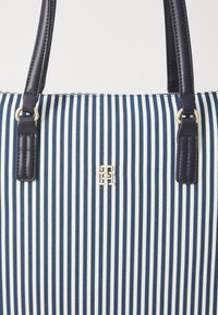 Sac fourre-tout rayé bleu marine et blanc en toile, avec des poignées en simili cuir et un emblème logo doré à l'avant.