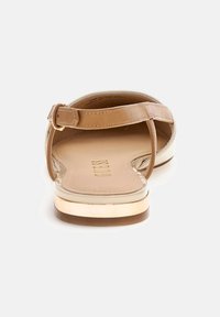 Barna szandál, lapos talppal, egyetlen pánttal az ujjak felett, állítható bokapánttal és arany színű díszítéssel az alján.