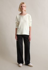 Leichtes Langarm-Henley-Shirt in Creme mit Knopfdetails, kombiniert mit schwarzen, weit geschnittenen Hosen und weißen Sneakern. Schlicht und leger geschnitten.