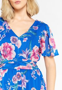 Modré květinové šaty s krátkými rukávy, hlubokým výstřihem do V a nařaseným pasem. Texturovaná látka s růžovými a fialovými květinovými vzory.