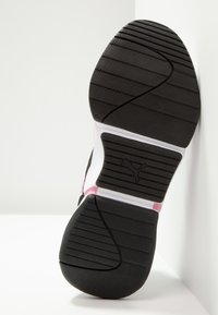 Black rubber sole of a sneaker with textured grip, white midsole, pink accents, and a puma logo in the center on a white background.