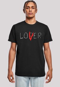 Černé bavlněné tričko s nápisem "LOVER" ve stylizovaném bílém a červeném písmu. Volný střih, krátké rukávy a kulatý výstřih.