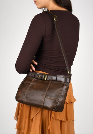 Bolso de hombro de cuero marrón con un diseño estructurado, que cuenta con un acento de cinturón y una correa ajustable, sobre una falda naranja en capas.