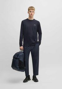 Navy long-sleeve shirt with logo, matching navy trousers, and a blue-black backpack. Model wears black sneakers. Simple and modern design.