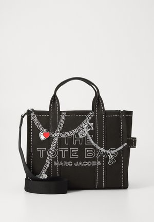 Geantă de tote din pânză neagră cu cusături albe, având un design cu lanț și farmecuri decorative, etichetată "THE TOTE BAG MARC JACOBS." Curea detașabilă.
