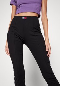 Černé ribbed kalhoty s vysokým pasem a viditelnou nášivkou "Tommy Jeans". Tkanina má hladkou texturu a střih na míru.