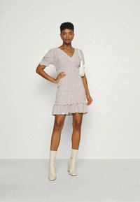 Vestido envolvente cinza com estampa floral, mangas bufantes, bainha de babados e tecido suave. Combinado com botas de tornozelo cremadas e uma pequena bolsa branca.