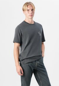 Short-sleeve, charcoal gray T-shirt in soft cotton with a round neckline, featuring a subtle graphic detail on the left chest.
