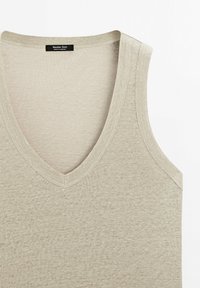 Jasnobeżowy top na ramiączkach z dekoltem w serek, wykonany z miękkiego materiału o gładkiej fakturze i minimalnych szwach. Etykieta z napisem "Massimo Dutti".