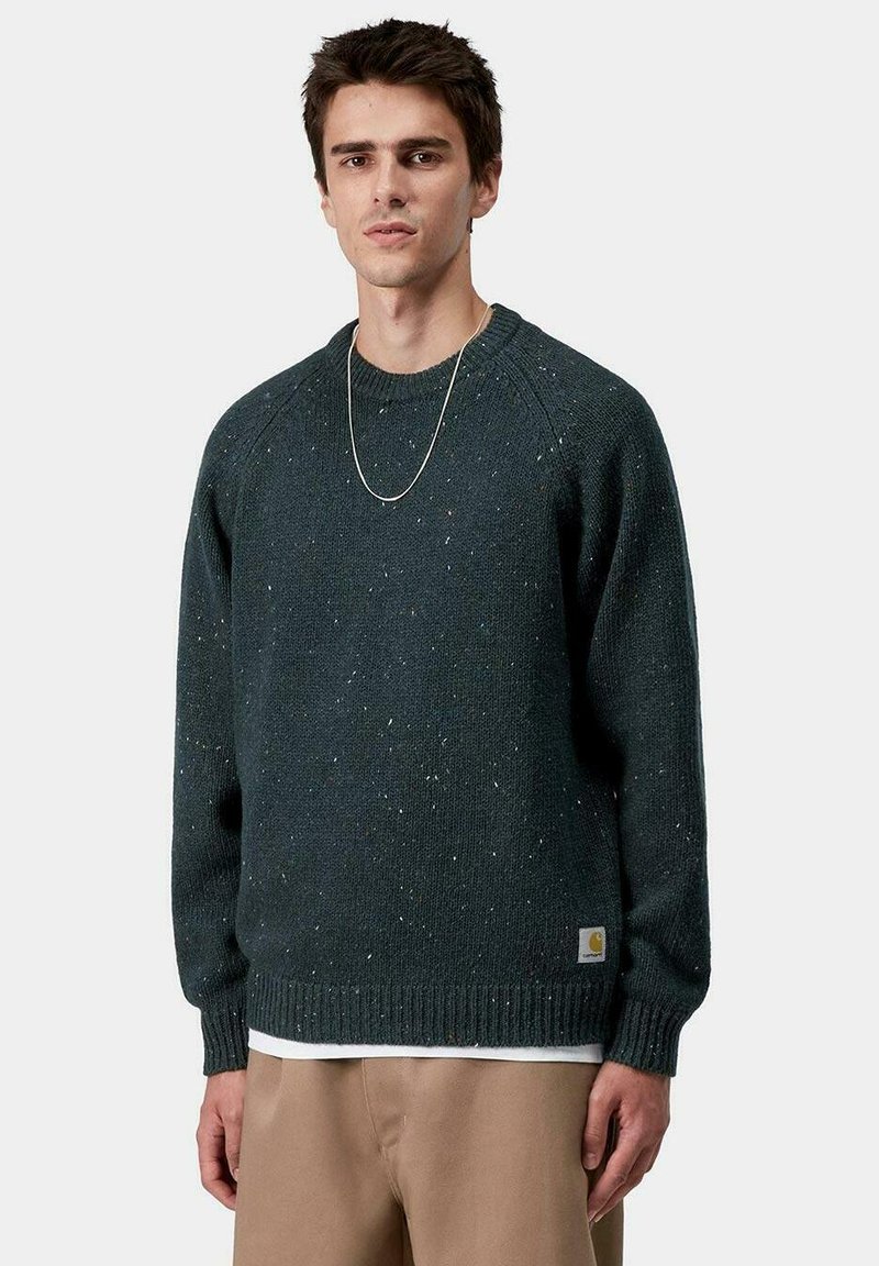 Maglione lavorato a maglia verde scuro con orlo e polsini a coste, caratterizzato da paillettes multicolori. Una piccola etichetta con logo in basso a sinistra.