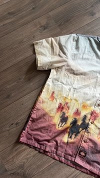 Īsām piedurknēm krekliņš bēšā krāsā, pārejot uz sarkaniem toņiem ar zirgus atgādinošām siluetēm. Saburzīta tekstūra un pogu detaļas priekšpusē.