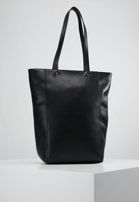 Czarna torba typu tote wykonana ze skóry, o eleganckim designie, z dwoma długimi uchwytami, prostym kształtem i minimalnymi detalami szwów.