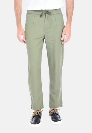 Pantaloni khaki con una vestibilità rilassata, pieghe davanti, vita con cordino e texture liscia; abbinati a sneakers nere con lacci gialli.