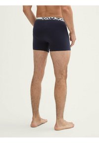 Boxeurs en coton bleu marine avec une ceinture élastique blanche contrastante arborant le nom de la marque. Texture douce et design ajusté.