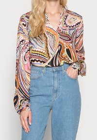 Blusa multicolore a maniche lunghe con motivo a spirale, dotata di colletto a carreggiata e maniche con polsini, abbinata a jeans a vita alta di colore azzurro chiaro.