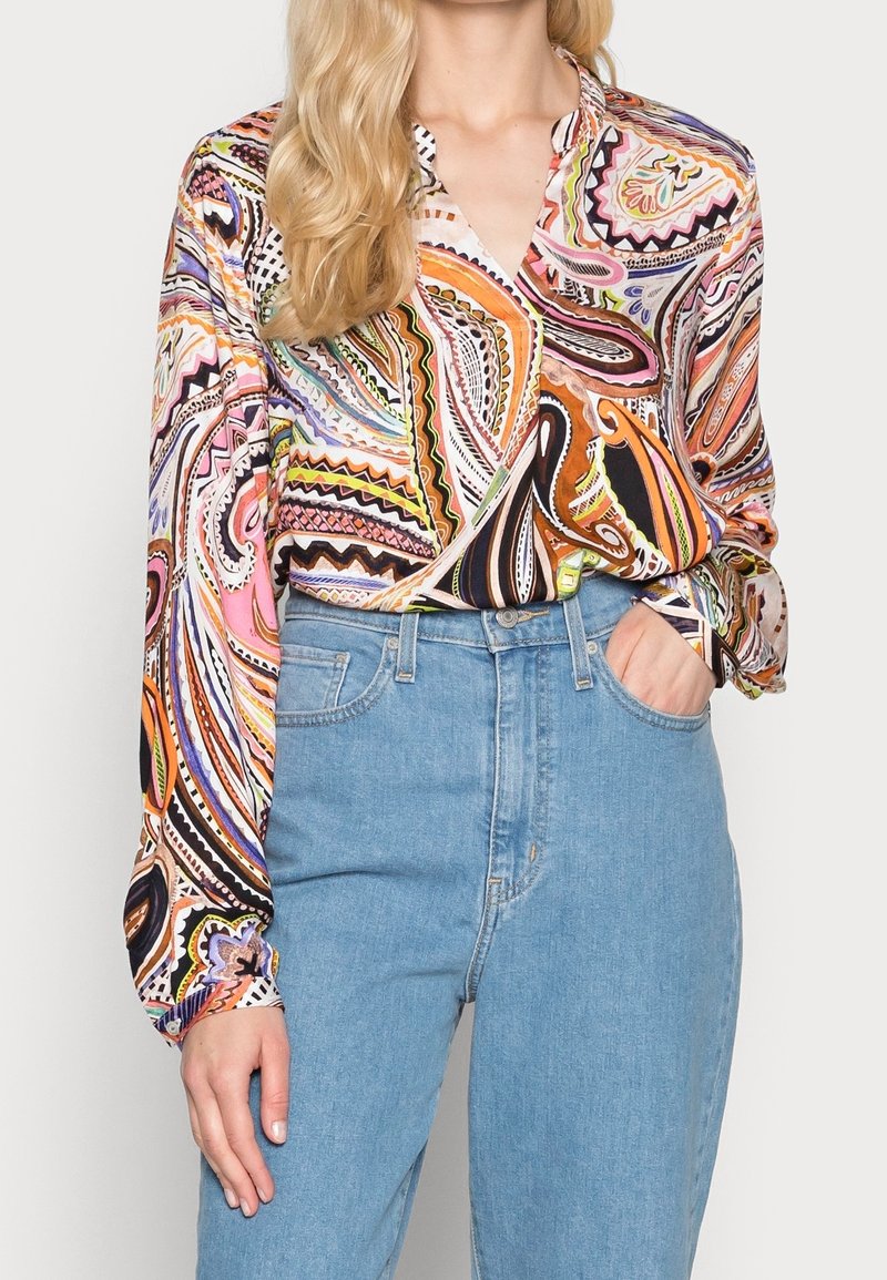 Blusa multicolore a maniche lunghe con motivo a spirale, dotata di colletto a carreggiata e maniche con polsini, abbinata a jeans a vita alta di colore azzurro chiaro.