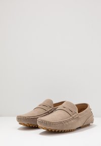 Beige suede loafers with a moccasin design, featuring stitched detailing and rubber outsole, provide a soft texture and casual look.