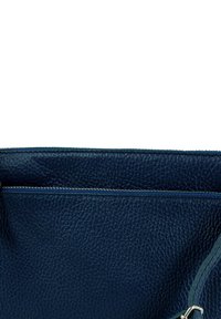 Marineblauwe leren handtas met een getextureerd oppervlak; voorzien van een bovenritssluiting en een zilverkleurige metalen accent voor het bevestigen van de riem.