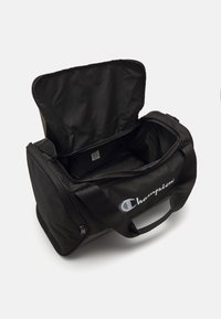 Borsa a sacco nera con apertura con zip. Realizzata in tessuto resistente, presenta il logo Champion in bianco ed è dotata di spallacci regolabili per un trasporto facile.