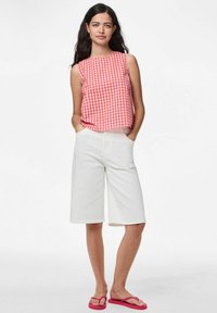 Červený a bílý kostkovaný bezrukávový top spárovaný s bílými šortkami po kolena a růžovými žabkami. Tento outfit má uvolněný střih.