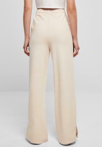 Lys beige vide bukser med elastisk liv og sidesplitter i kanten, laget av myk, strukturert stoff.