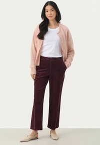 Lichtroze cardigan, witte t-shirt en bordeaux corduroy broek. De cardigan heeft knopen; de broek heeft een verticale textuur. Beige ballerina's maken de outfit af.