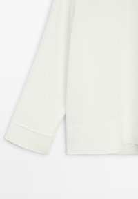 Bílý široký top s kulatým lemem a tříčtvrtečními rukávy s manžetami. Vyrobený z hladké, lehké látky s jemnou texturou.