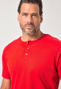 Rotes Henley-Shirt mit kurzen Ärmeln, rundem Ausschnitt und Dreiknopf-Leiste. Weicher, glatter Stoff ohne sichtbare Muster oder Akzente.