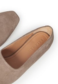 Grå mockaskor med spetsig tå, med en tan läderinnersula. Designen är minimalistisk med slät yta och rena linjer.