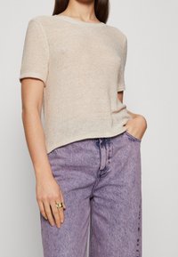 Lichtbeige gebreide top met korte mouwen en een ronde halslijn, gecombineerd met hoogtaille paarse jeans die iets vervaagd zijn. Soepele textuur, relaxte pasvorm.