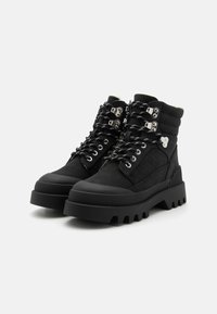 Bottes noires mi-hautes en tissu texturé avec des semelles en caoutchouc épaisses, dotées d'œillets en métal, de détails en lacets et de poignets rembourrés.