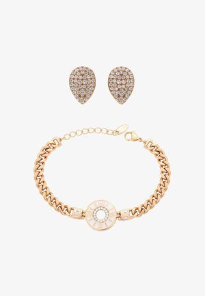 Goldenes Gliederarmband mit einem Uhranhänger im römischen Ziffern-Design und tropfenförmigen, mit Diamanten besetzten Ohrringen auf weißem Hintergrund.