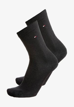 Chaussettes en coton noires avec des bords côtelés, arborant un petit logo rouge, blanc et bleu. Texture lisse et design de hauteur moyenne.
