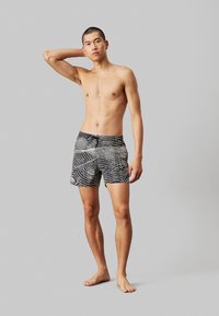 Costume da bagno a righe bianche e nere con vestibilità comoda, dotati di vita regolabile con lacci e un tessuto leggero e morbido.