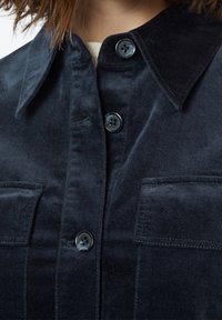 Tmavě námořnická košile na knoflíky z měkké manšestrové látky, s špičatým límečkem, dvěma kapsami na prsou a čtyřmi černými knoflíky.