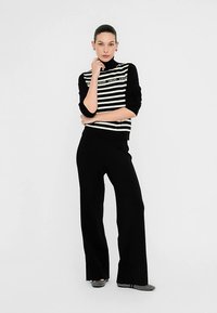 Črno-beli pulover z visokim ovratnikom s črtastim vzorcem in detajlom logotipa, kombiniran s črnimi širokimi hlačami. Gladek tekstura in oprijeta silhueta.