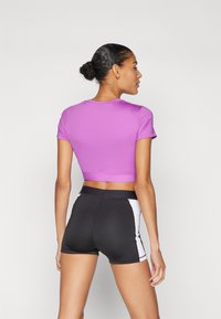 Lilla lühikeste varrukatega sporttop mustade lühikesed püksid, millel on valged külgpaneelid. Kangas näeb välja sile ning sobib hästi.
