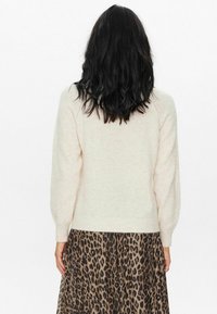 Krémový pletený sveter s vyp puffovými rukávmi, skombinovaný s sukňou s leopardím vzorom. Sveter má rebrovaný lem a manžety.